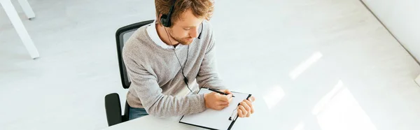 Panoramic shot of bearded operator in brokers agency writing while holding clipboard — Stock Photo