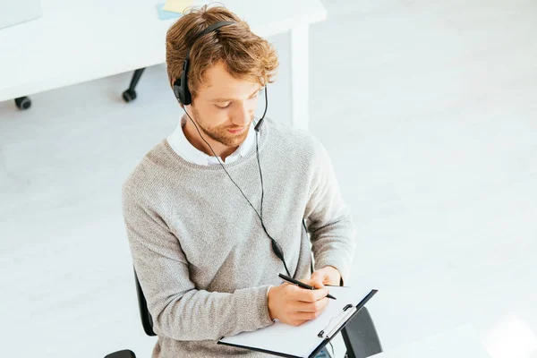 Handsome bearded operator in brokers agency writing while holding clipboard — Stock Photo