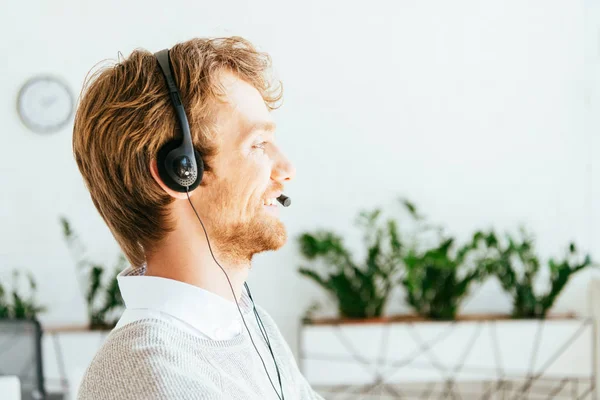 Seitenansicht des glücklichen und bärtigen Bedieners in Makleragentur mit Headset — Stockfoto