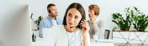 Colpo panoramico di attraente broker toccando auricolare vicino ai colleghi in ufficio — Foto stock