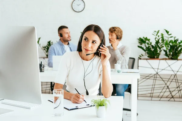 Messa a fuoco selettiva di broker attraente con penna toccare auricolare vicino ai colleghi — Foto stock