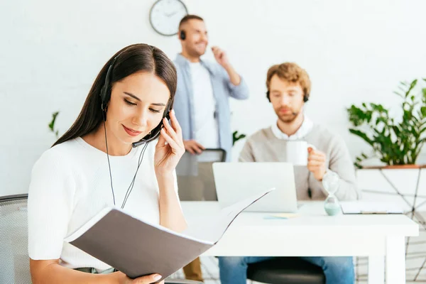 Selective focus of happy broker looking at folder near coworkers in office — Stock Photo