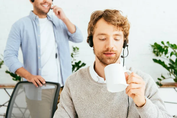 Selective focus of handsome bearded broker holding cup near coworker in office — Stock Photo