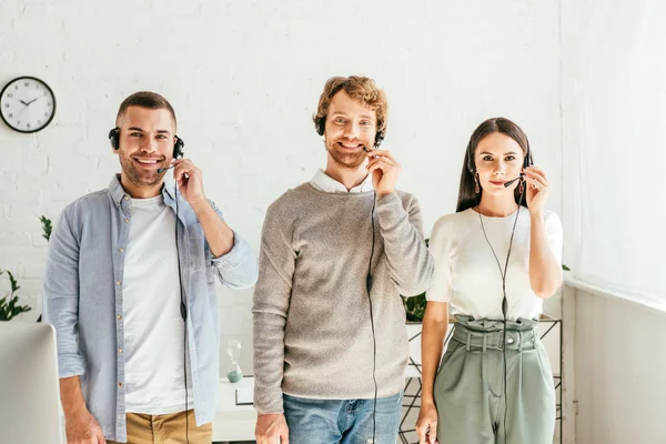 Cheerful brokers in headsets standing and looking at camera — Stock Photo
