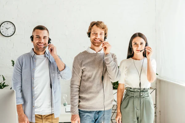 Brokers alegres en auriculares de pie y mirando a la cámara - foto de stock