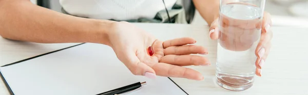 Panoramic shot of broker holding pill and glass of water in office — Stock Photo