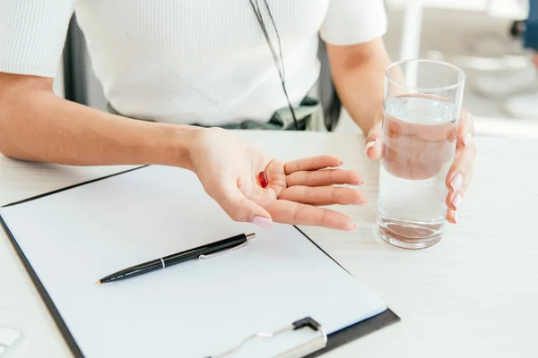 Cropped view of broker holding pill and glass of water in office — Stock Photo
