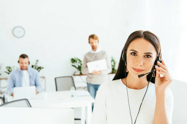 Selective focus of beautiful broker touching headset while working with coworkers — Stock Photo