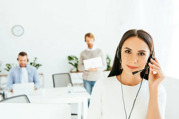 Selektive Fokussierung des schönen Maklers auf das Headset während der Arbeit mit Mitarbeitern — Stockfoto