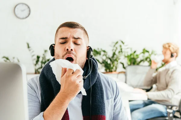 Selective focus of diseased broker sneezing in tissue near coworker in office — Stock Photo