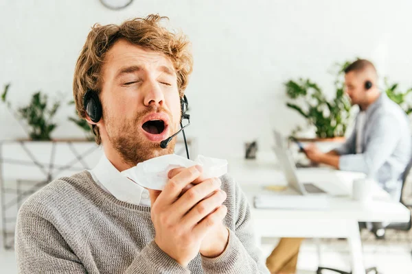 Sick bearded broker with closed eyes sneezing near coworker in office — Stock Photo