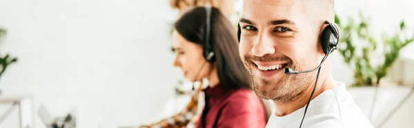 Panoramic shot of cheerful broker in headset working in office with coworkers — Stock Photo