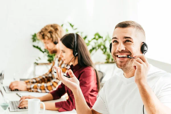 Foyer sélectif de courtier joyeux dans la gestuelle casque au bureau avec des collègues — Photo de stock