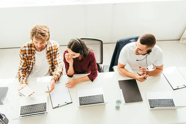 Ansicht von Makler hält Taschenrechner in der Nähe von Frau im Headset und Mitarbeiter im Call Center — Stockfoto