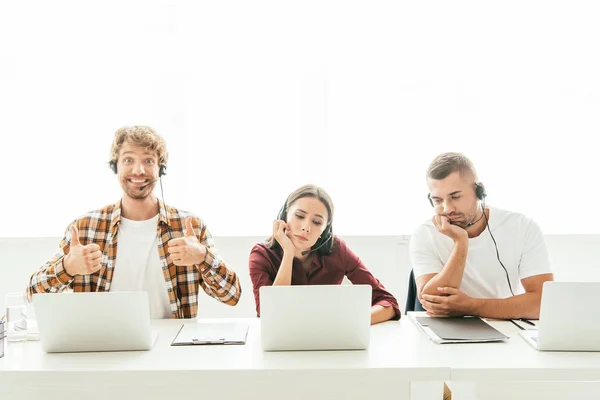 Happy broker showing thumbs up near sad coworkers in call center — Stock Photo