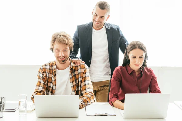 Felice broker in piedi vicino agli operatori con auricolari in call center — Foto stock