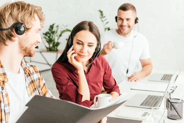 Selektiver Fokus des bärtigen Maklers, der Ordner in der Nähe von Frau und Mitarbeiterin im Büro hält — Stockfoto