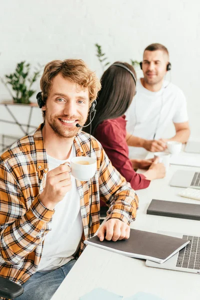 Selective focus of happy bearded broker holding cup of coffee near coworkers — Stock Photo