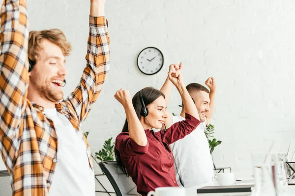 Selective focus of happy brokers with hands above heads in office — Stock Photo