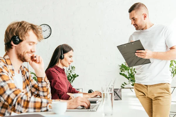 Selective focus of broker holding clipboard near operators in office — Stock Photo