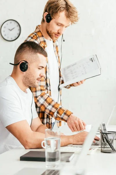 Handsome broker standing with notebook near coworker in headset — Stock Photo