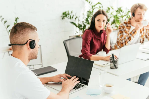 Selective focus of broker typing on laptop keyboard near coworkers in office — Stock Photo