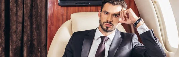Panoramic shot of pensive businessman in suit looking at camera in private plane — Stock Photo