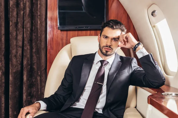 Nachdenklicher Geschäftsmann im Anzug blickt im Privatflugzeug in die Kamera — Stockfoto