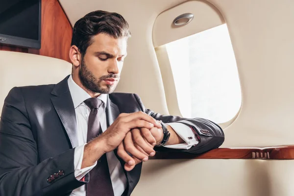 Apuesto hombre de negocios de traje mirando el reloj de pulsera en avión privado - foto de stock