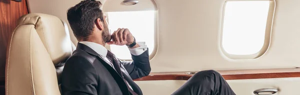 Tiro panorâmico de homem de negócios no terno que olha pela janela no avião privado — Fotografia de Stock