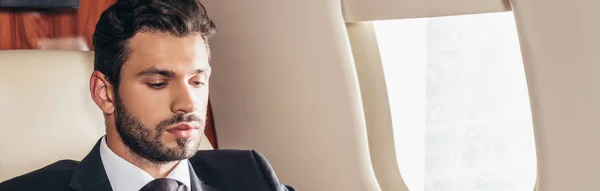 Colpo panoramico di bell'uomo d'affari in giacca e cravatta guardando giù in aereo privato — Foto stock
