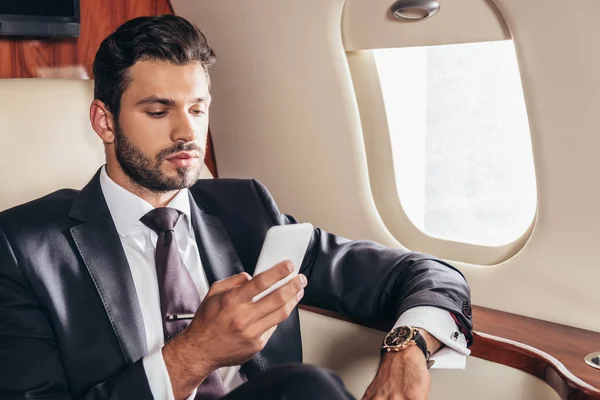 Homem de negócios bonito em terno usando smartphone em avião privado — Fotografia de Stock