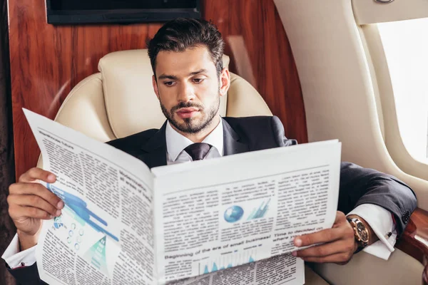 Handsome businessman in suit reading newspaper in private plane — Stock Photo