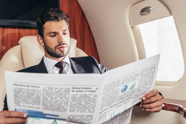 Bonito empresário no terno ler jornal no avião privado — Fotografia de Stock