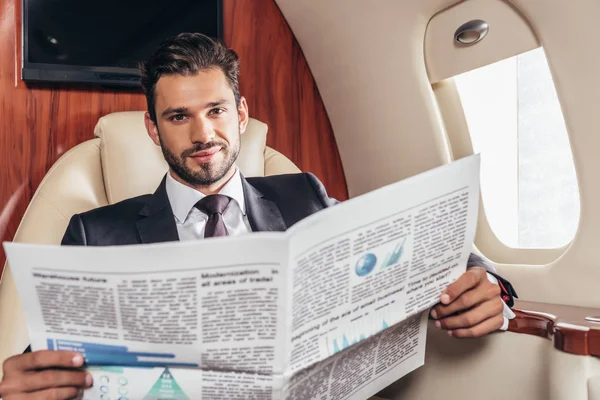 Handsome businessman in suit holding newspaper in private plane — Stock Photo