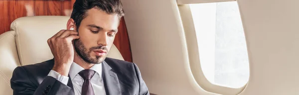 Plano panorámico de hombre de negocios guapo en traje escuchando música en avión privado - foto de stock