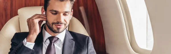 Panoramic shot of handsome businessman in suit listening music in private plane — Stock Photo