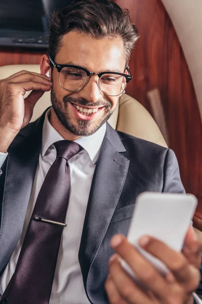 Focalizzazione selettiva di un uomo d'affari sorridente che ascolta musica e utilizza lo smartphone in aereo privato — Foto stock