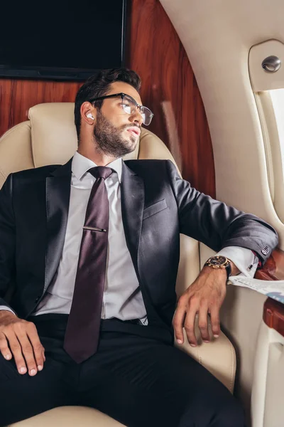 Guapo hombre de negocios en traje escuchando música en avión privado - foto de stock