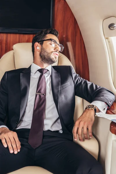 Bel homme d'affaires en costume dormir et écouter de la musique en avion privé — Photo de stock