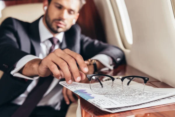 Enfoque selectivo guapo hombre de negocios en traje tomando gafas en avión privado — Stock Photo