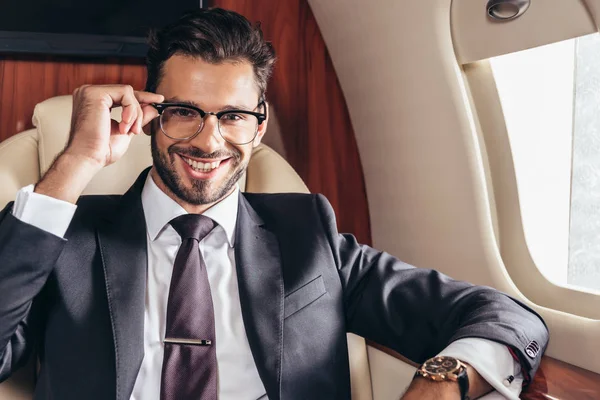 Schöner Geschäftsmann mit Brille, der im Privatflugzeug lächelnd in die Kamera blickt — Stockfoto