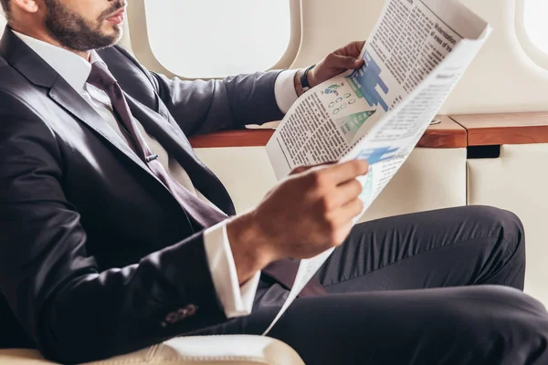 Visão cortada de empresário em terno jornal de leitura em avião privado — Fotografia de Stock