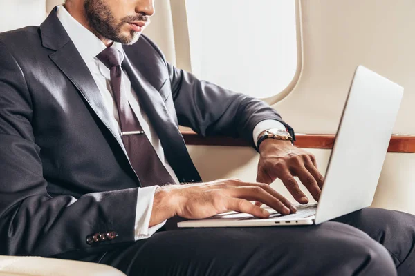 Cropped view of businessman in suit using laptop in private plane — Stock Photo