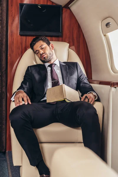 Handsome businessman in suit with book sleeping in private plane — Stock Photo