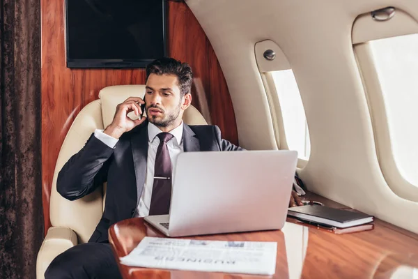 Guapo hombre de negocios en traje hablando en smartphone en avión privado - foto de stock