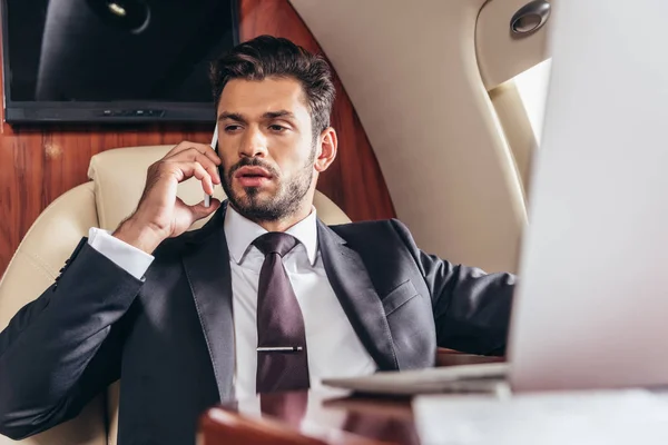 Красивый бизнесмен в костюме разговаривает по смартфону в частном самолете — стоковое фото