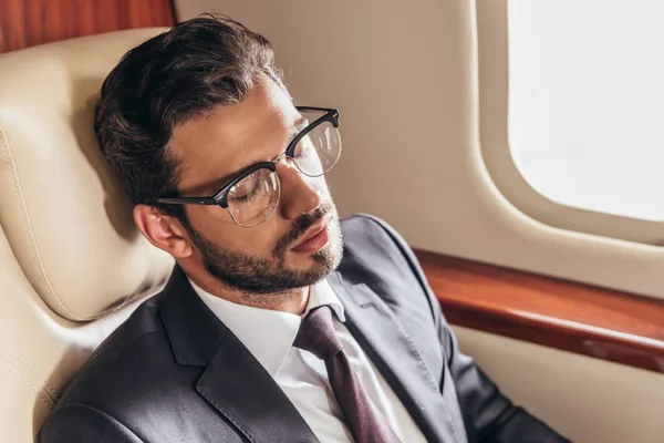 Bel homme d'affaires en costume et lunettes dormant dans un avion privé — Photo de stock