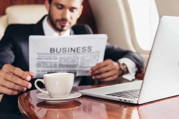 Избирательное внимание бизнесмена в костюме читающего деловую газету и принимающего кубок в частном самолете — стоковое фото