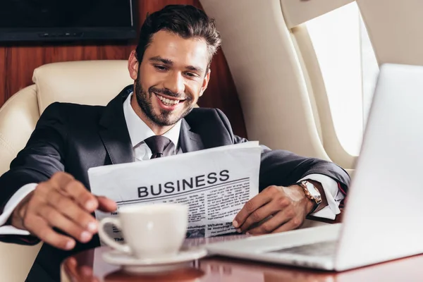 Foyer sélectif de sourire homme d'affaires en costume avec journal prendre tasse en avion privé — Photo de stock